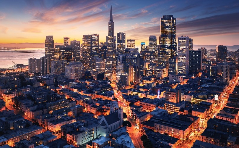 夕暮れの都市 奥には高層ビルの窓の明かり 手前には街灯や建物の窓の明かりで照らされている住宅街