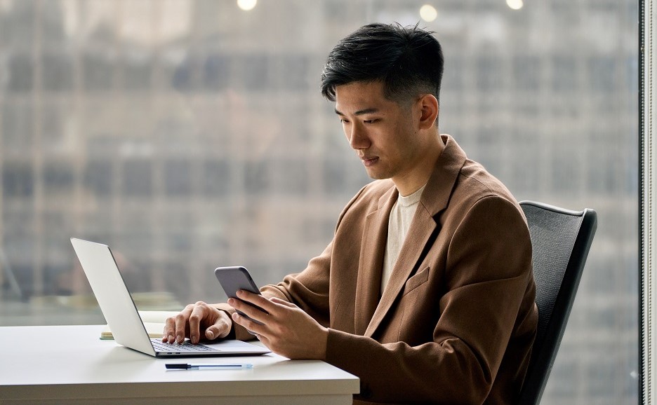 ノートPCを前にスマートフォンを確認する男性