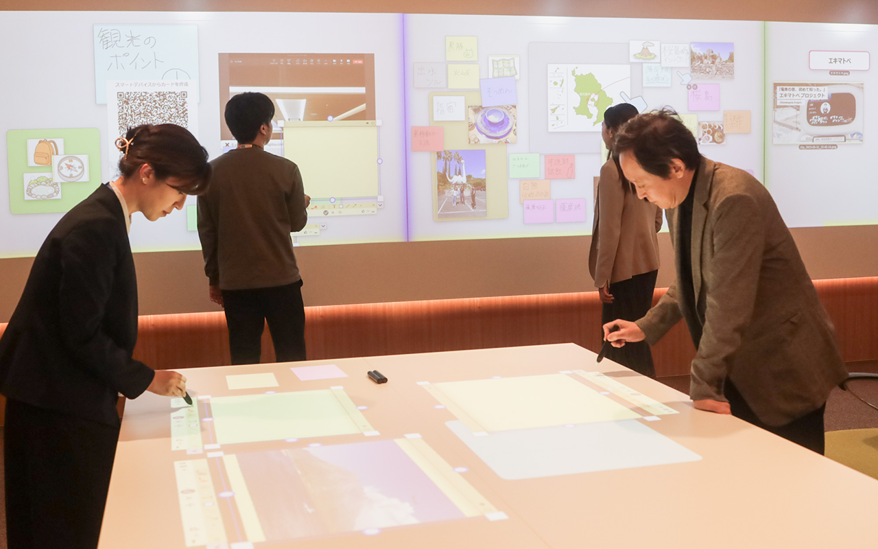 会議デスクに映し出された資料へ書き込みする２人