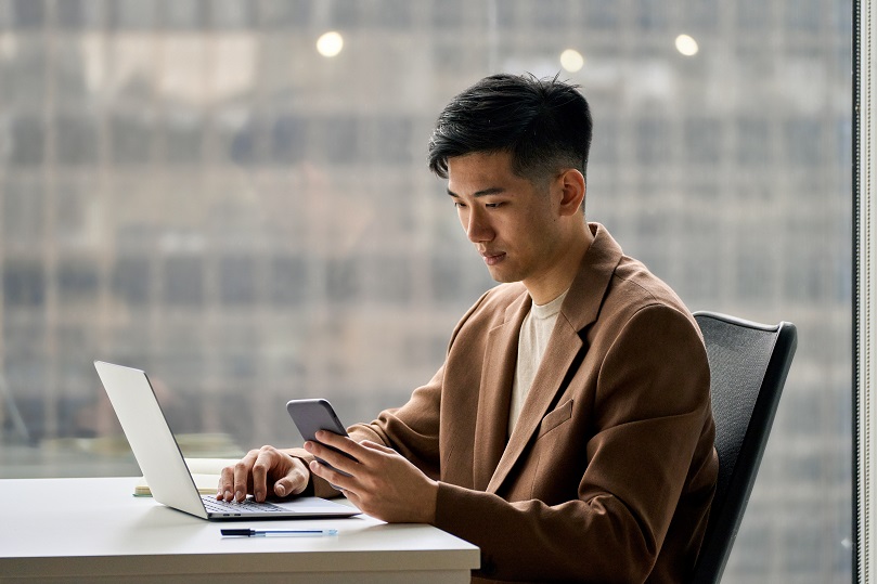 ノートPCを前にスマートフォンを確認する男性