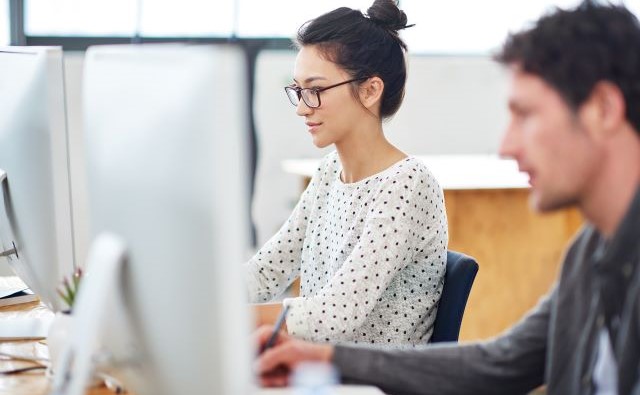 オフィスにいる男性と女性が、それぞれパソコンのモニターを見て作業をしている