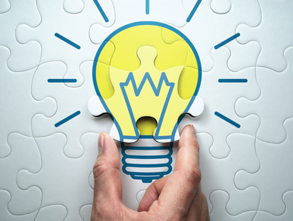 ジグソーパズルのピースに描かれた電球のイラストを持ち上げる指先