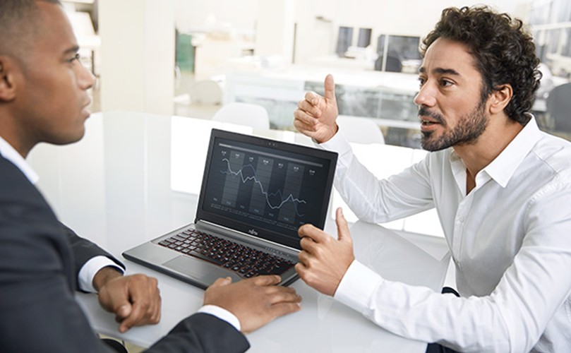  Two people in a business setting reviewing a laptop screen displaying a line graph with multiple data points