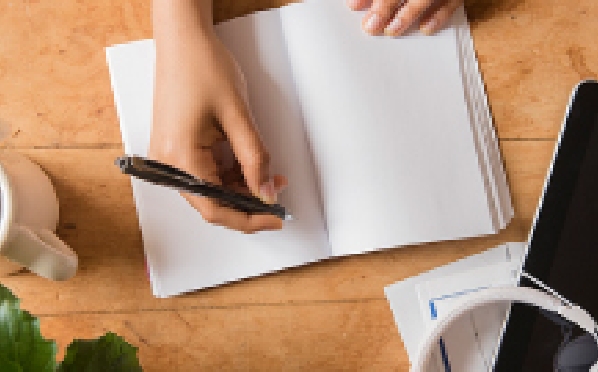 Draufsicht auf eine Hand, die in ein weißes Notizbuch schreiben möchte