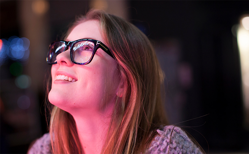 a photograph of a young woman with glasses looking up