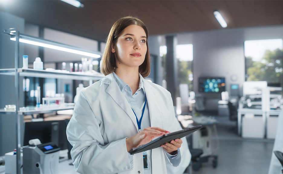 A woman researcher in a lab coat is operating a tablet in a laboratory.