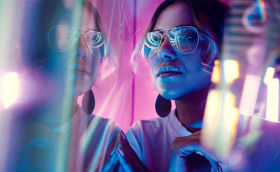 Woman in glasses standing in front of glass with neon reflections