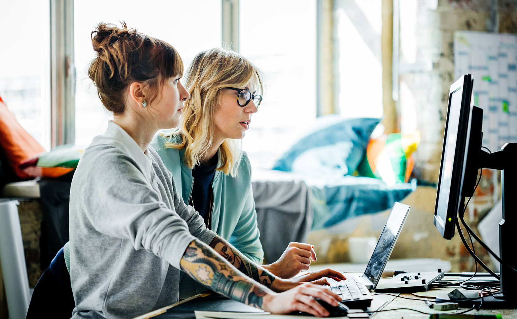 Two women looking to a computer monitor and a laptop