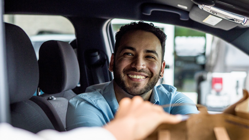 A man is receiving the goods through the window of the car in the drive-through