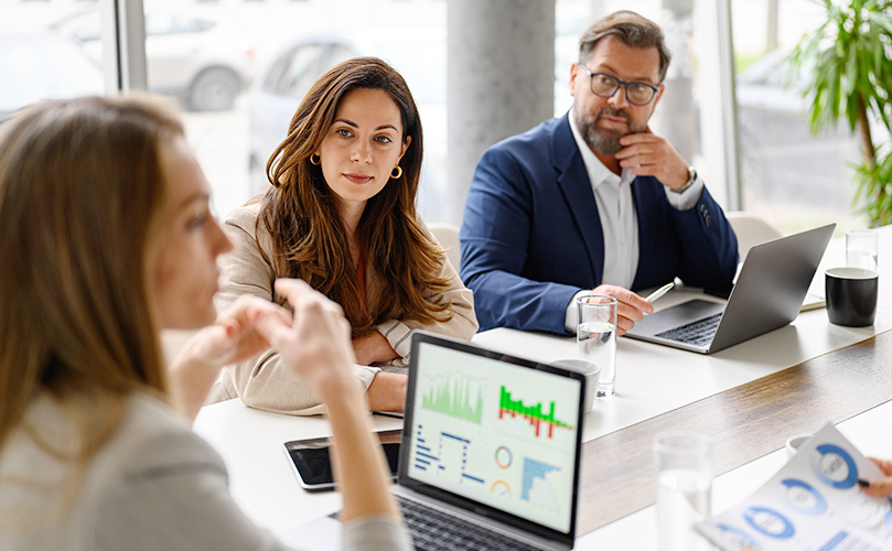 会議室でプレゼンを聞く3人、ラップトップにはグラフの写真