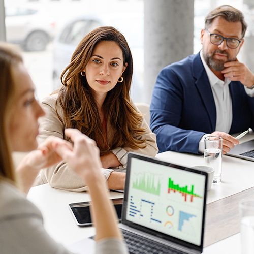 Three people in a meeting, laptop shows graphs photo.