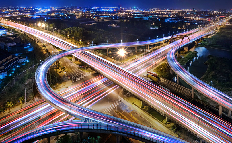 English ALT text: Night aerial view of highway junction with car light trails photo.