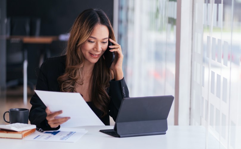 Portrait of a businesswoman talking on Smartphone while working at desk in office using laptop