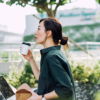 ノートパソコンとコーヒーを持ってオフィスの外に座っている女性