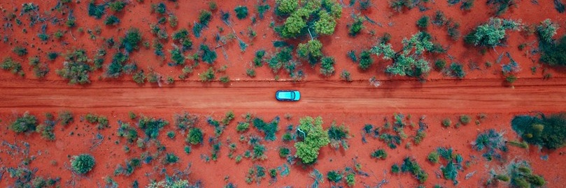 Aerial view of the Australian outback with a red dirt road and scattered green bushes.