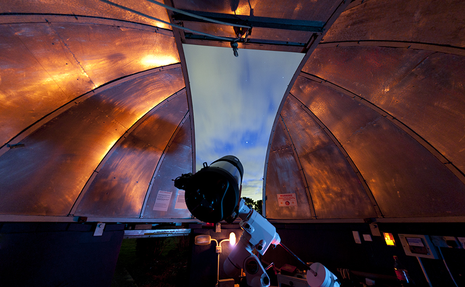 Inside an observatory dome with a telescope pointed at the night sky.