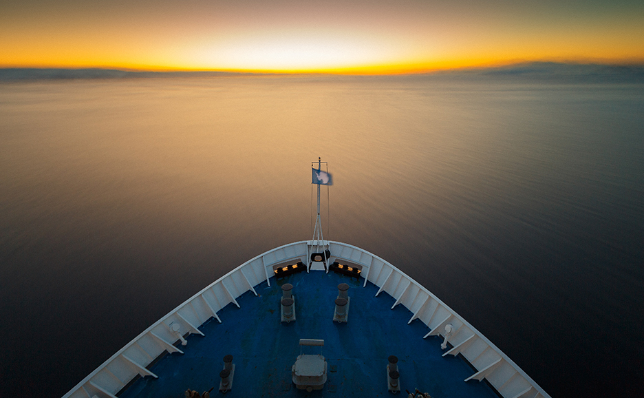 View from a ship's bow of the open sea and sunset on the horizon.